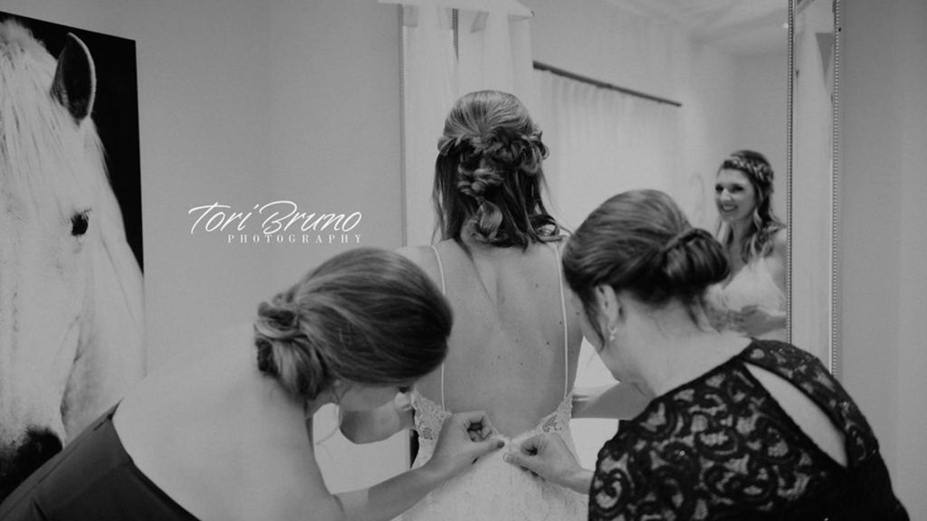 bridesmaids fasten wedding dress in suite at Palace Event Center | photo by Tori Bruno